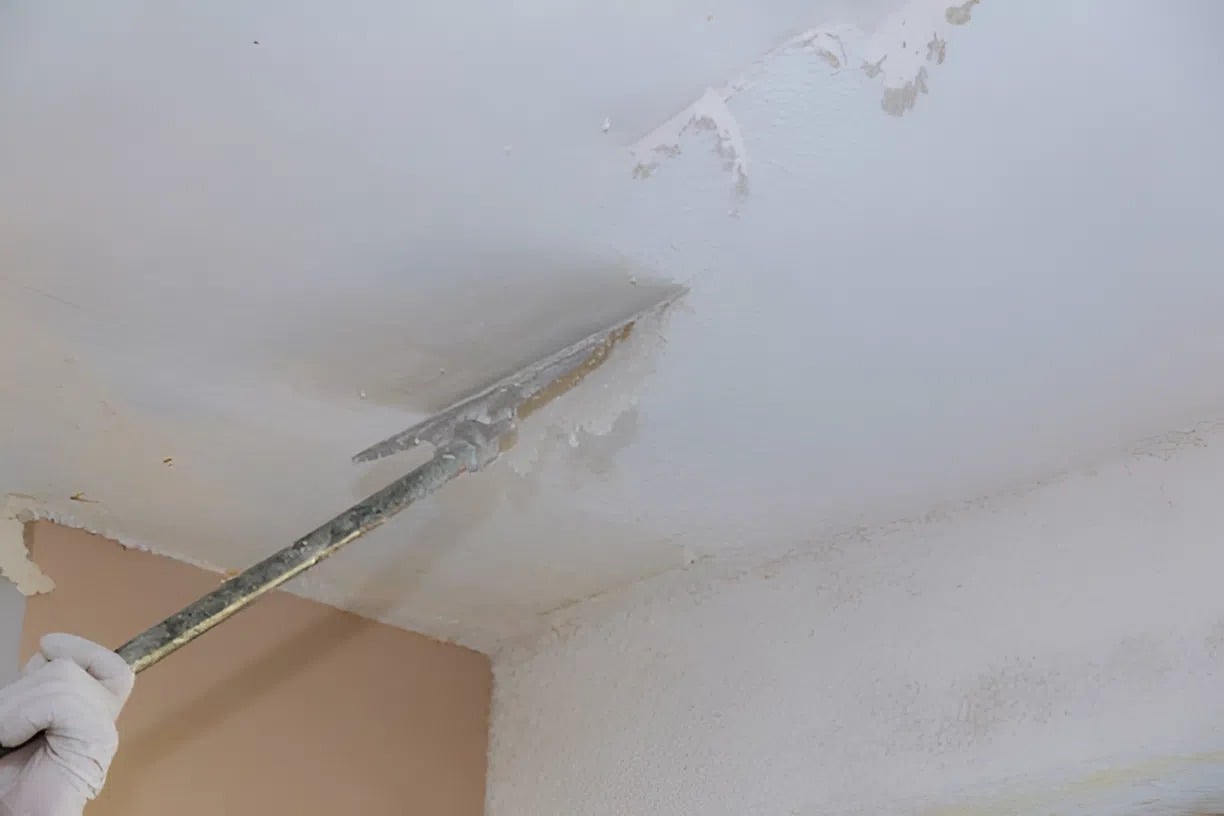 Professional painter in Kalamazoo, MI, removing popcorn ceiling texture with specialized tools for a smooth finish